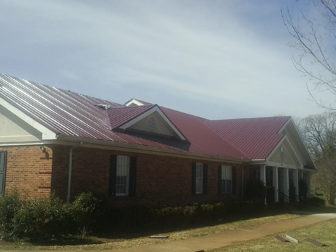 Red metal roof with gabled entries on a long brick building, from a Hail Damage Roof Repair job in Southampton